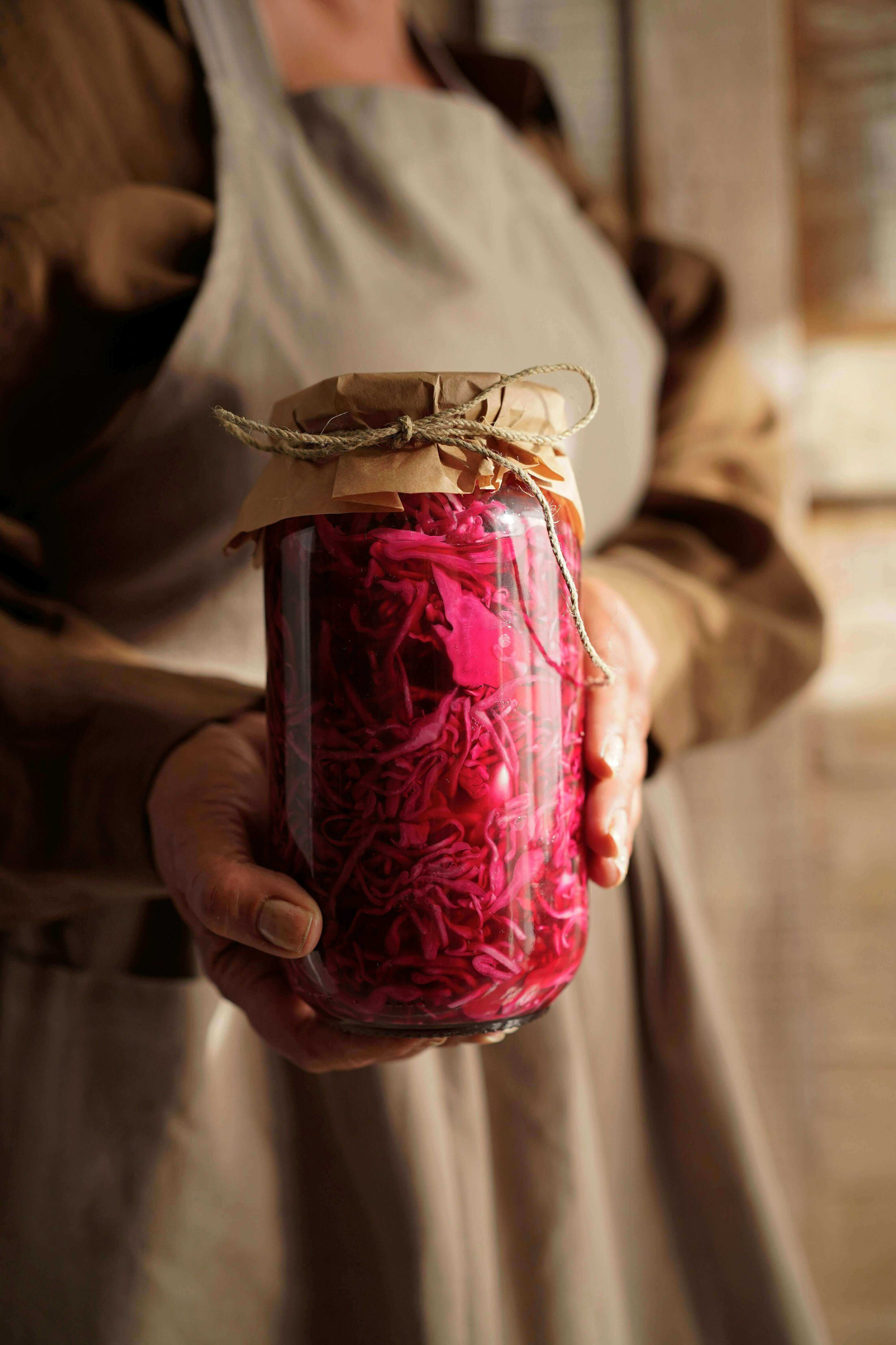 A person holding a jar filled with pink fermented vegetables, emphasizing digestive health matters: trust your gut - Windback NZ.