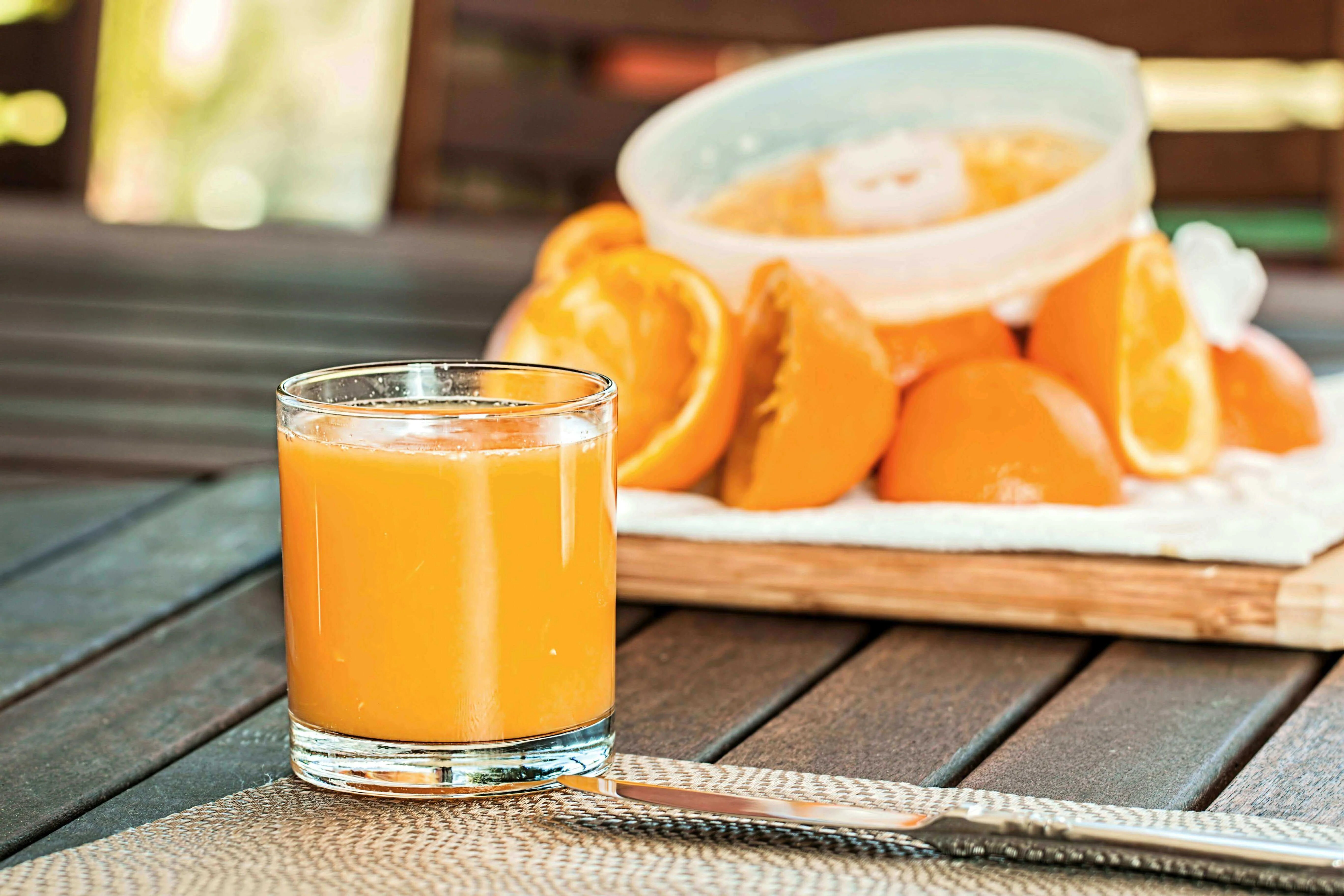 Glass of orange juice with fresh oranges in the background on a wooden table, symbolizing metabolic health and nutrition.