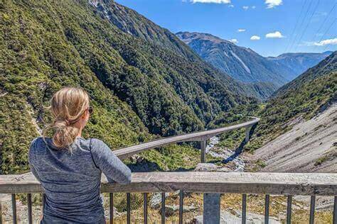 Person enjoying scenic view of mountainous landscape and valley with clear sky in the background.