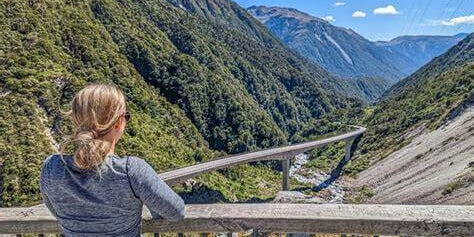 Person enjoying scenic view of mountainous landscape and valley with clear sky in the background.