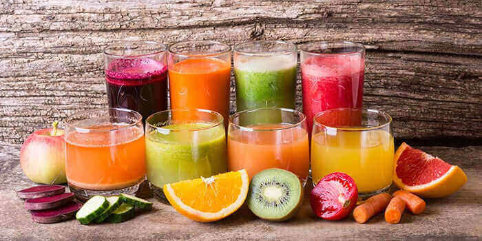 Colorful assortment of fresh fruit and vegetable juices in glasses on a rustic wooden background - Windback NZ