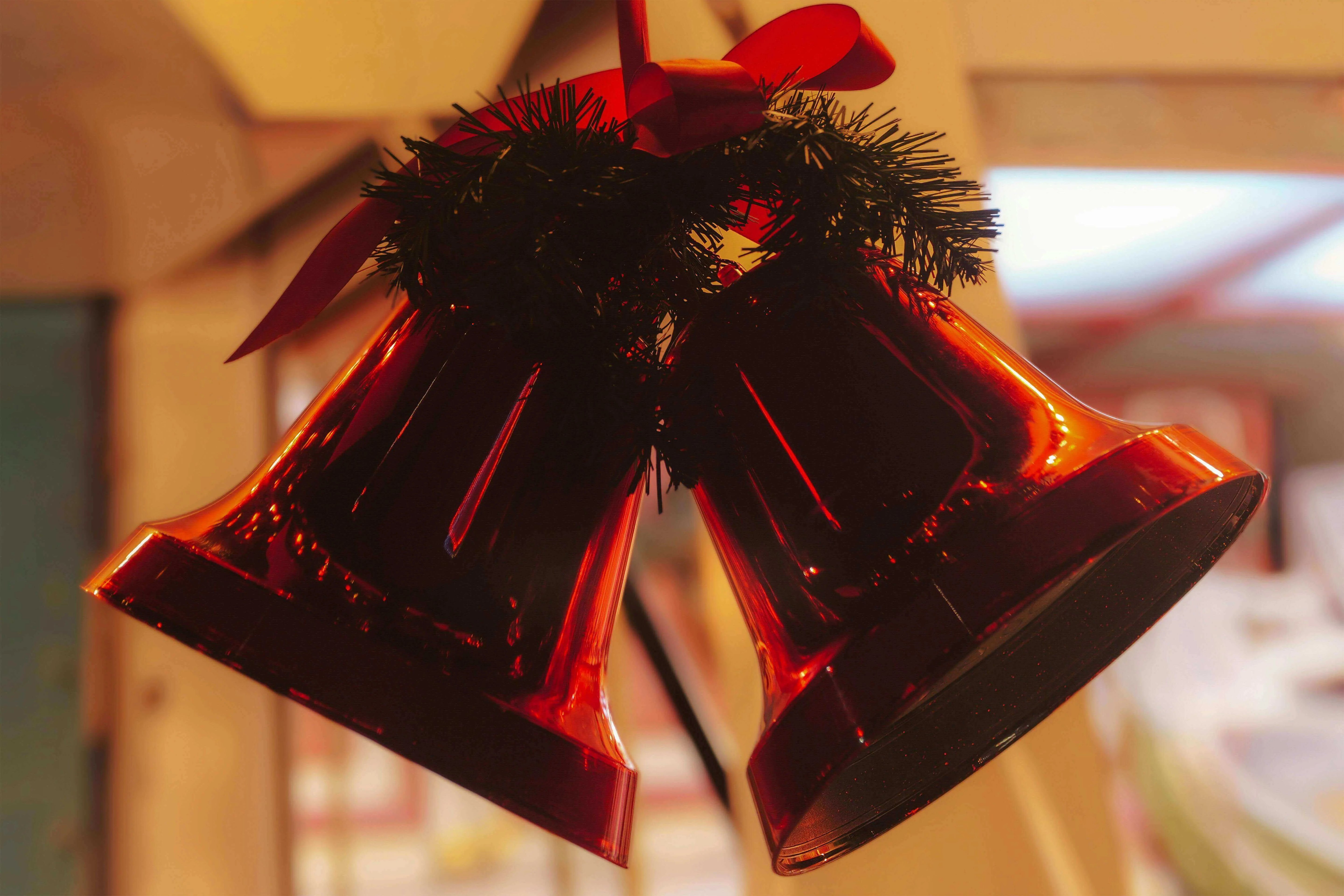 Two red holiday bells adorned with a green garland and a red ribbon, hanging decoratively.