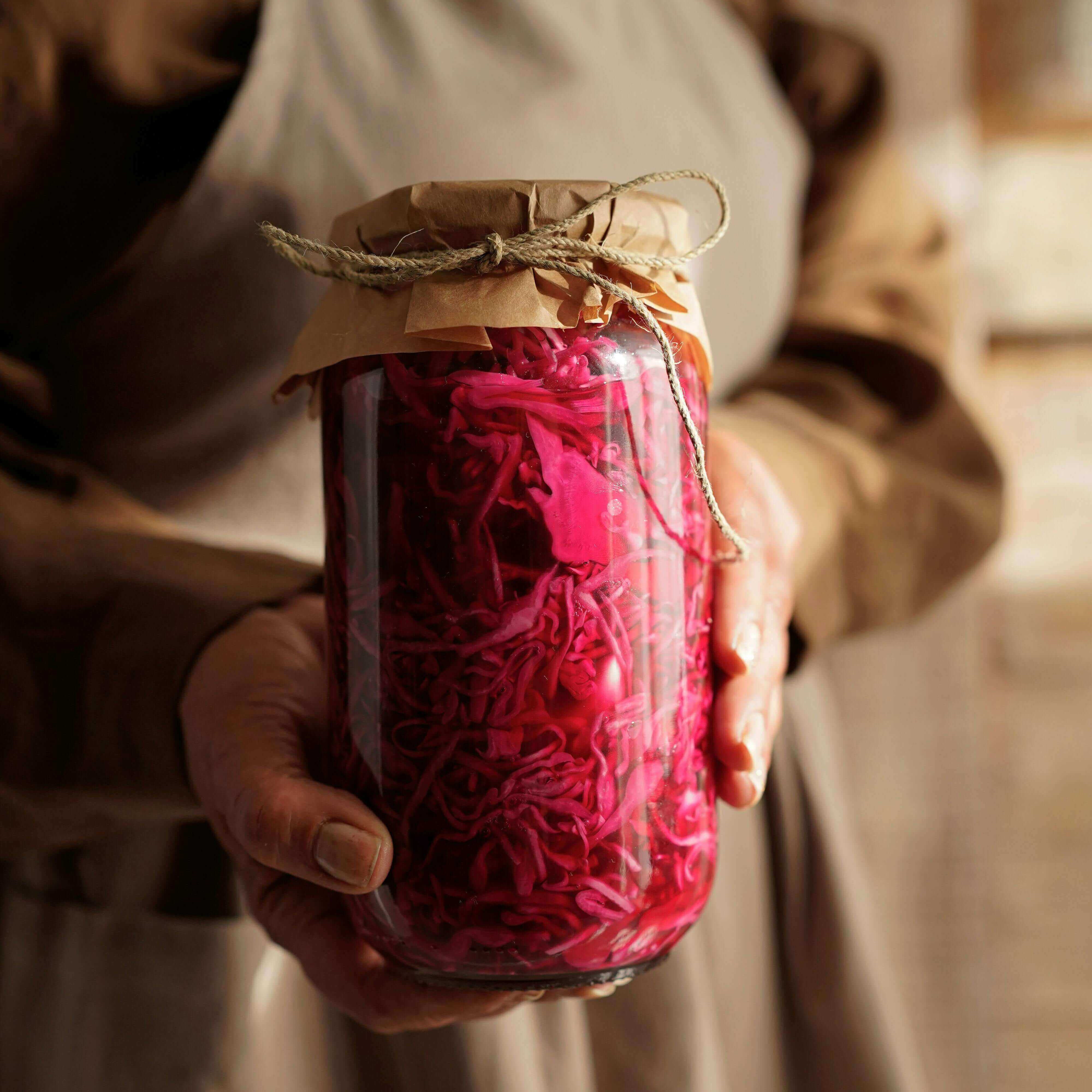 A person holding a jar filled with pink fermented vegetables, emphasizing digestive health matters: trust your gut - Windback NZ.