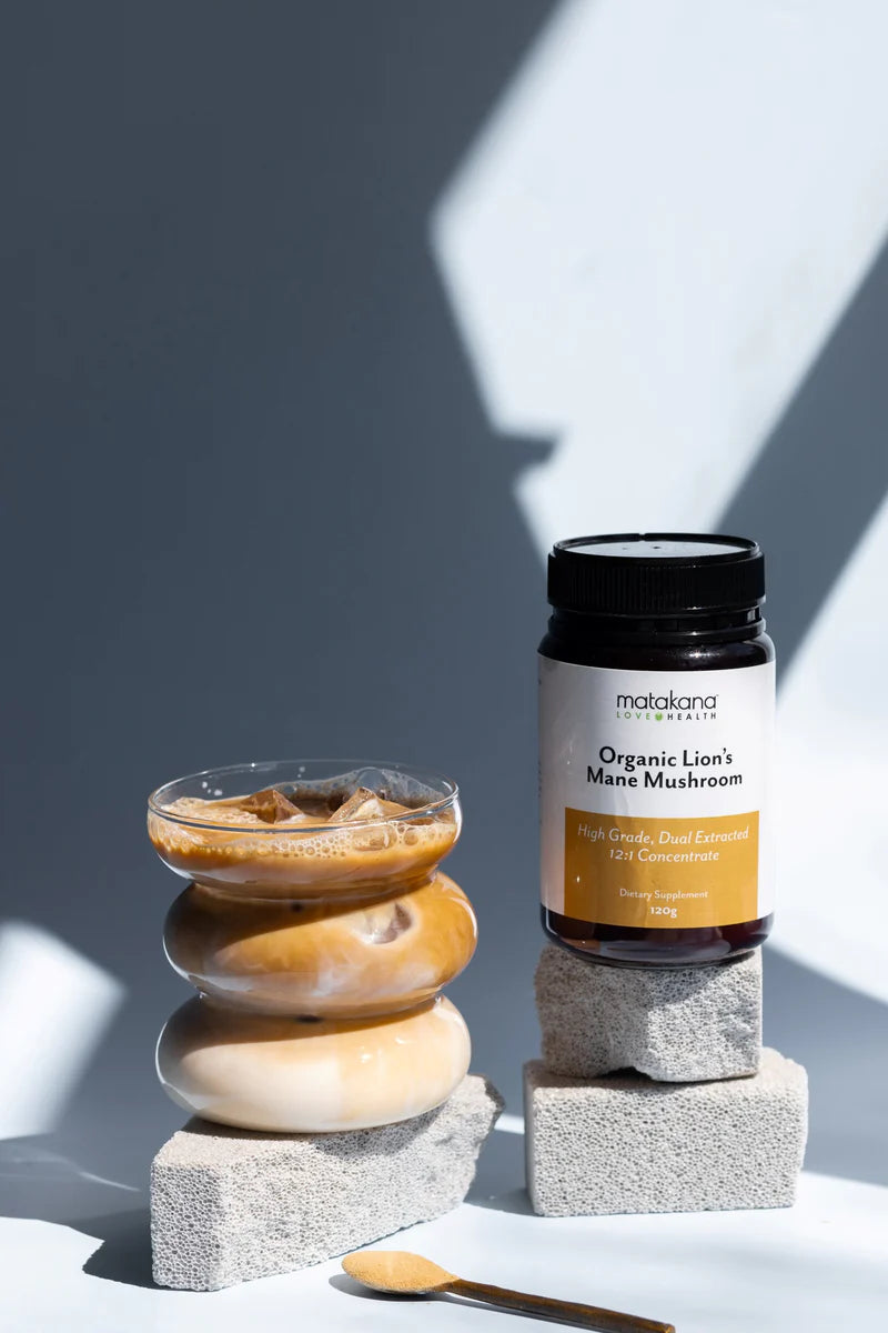 Matakana Superfoods Lion's Mane Mushroom Powder 120g with iced coffee in a glass and decorative stones.
