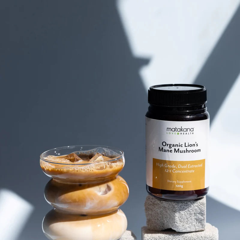 Matakana Superfoods Lion's Mane Mushroom Powder 120g with iced coffee in a glass and decorative stones.