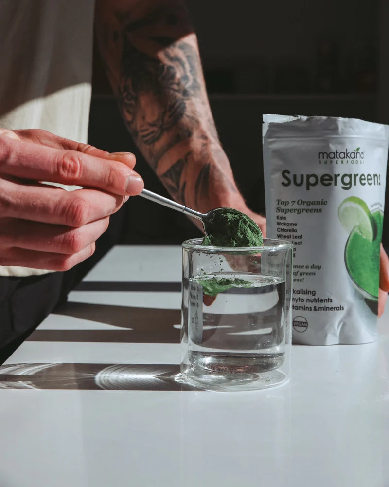 Matakana Superfoods Organic SuperGreens 200g powder being mixed in a glass of water.