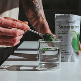 Matakana Superfoods Organic SuperGreens 200g powder being mixed in a glass of water.