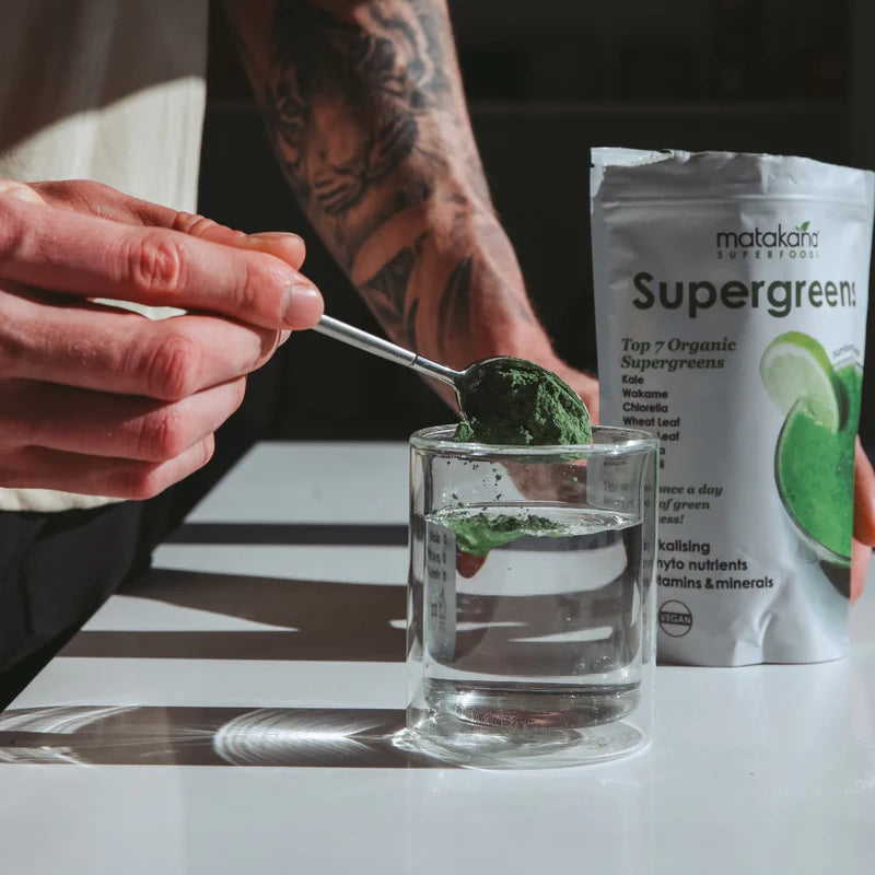 Matakana Superfoods Organic SuperGreens 200g powder being mixed in a glass of water.