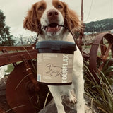 Dog holding a FourFlax probiotics container in its mouth outdoors.