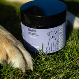 Jar labeled 'Calm' for dogs on grass with a dog's paw in the foreground
