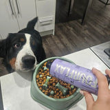 Dog looking at a bowl of food with a person holding a 'Fourflax' container in a kitchen.