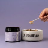 Person scooping Fourflax pet food from a bowl with a jar of Fourflax product on a purple background